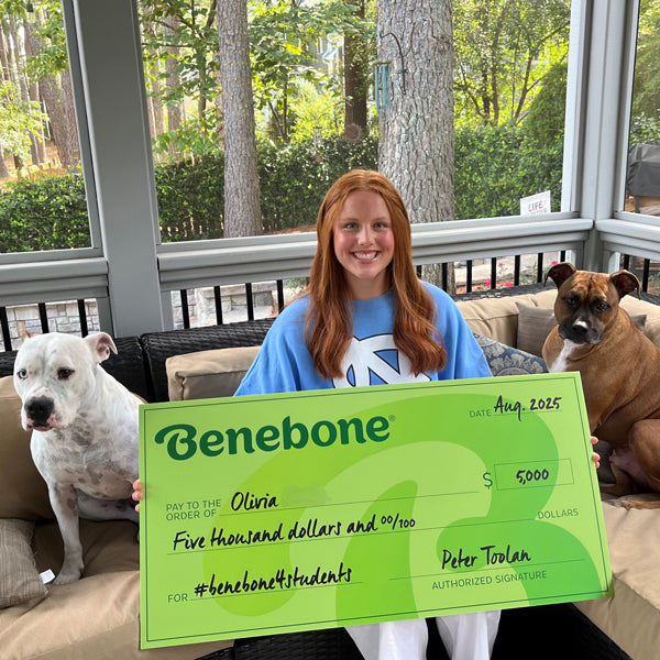 Benebone scholarship winner Olivia holding a large green check, sitting next to two dogs.