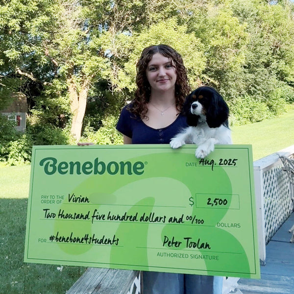 Benebone scholarship winner Vivian holding a large green check, standing outdoors with her dog.