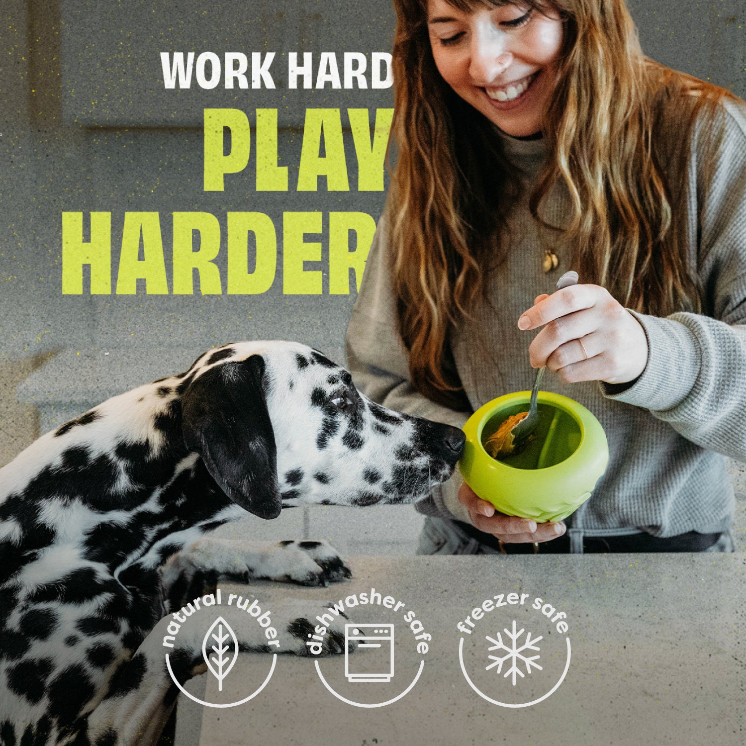 A woman smiles as she fills a green Benebone Chew & Treat Duo for her Dalmatian. Text reads “Work hard, play harder.” Icons show it’s made of natural rubber, dishwasher safe, and freezer safe.