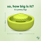 Green circular pet toy called the Benebone Tongue Twister, featuring a textured raised center and crafted from natural rubber as an interactive puzzle to support dog enrichment. Text reads, "So, how big is it? It's pretty big!" Measurements: 2.86 inches tall and 4.56 inches wide. Bustle logo in the bottom right corner on a pale green background.